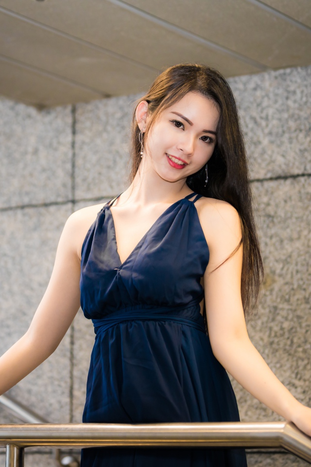 Красивая азиатка в черном платье стоит у перил