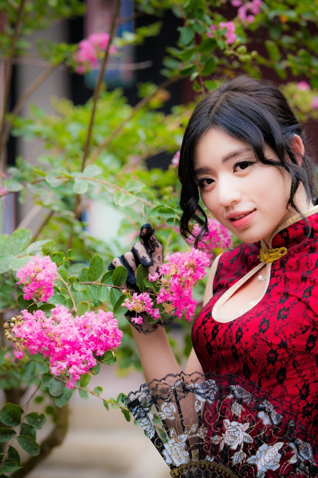 Красивая азиатка с веером в руках стоит у куста с розовыми цветами