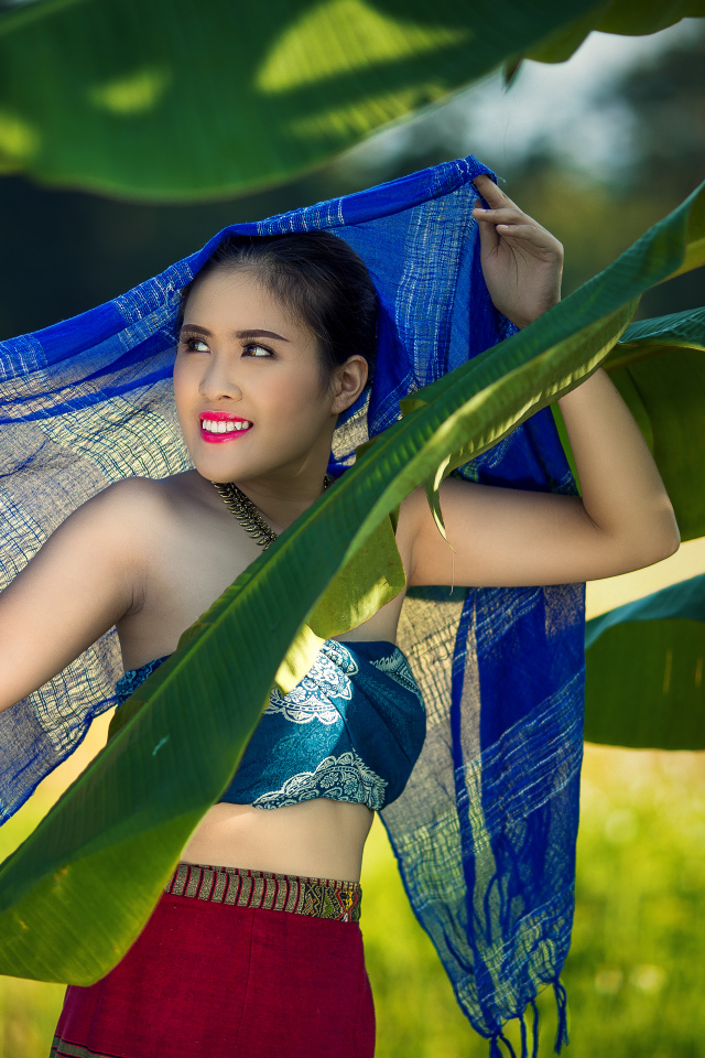 Красивая девушка азиатка с синим палантином у зеленых листьев