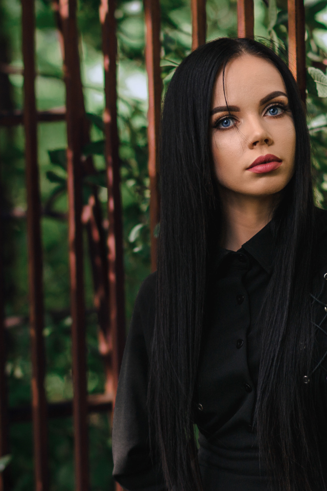 Красивая голубоглазая девушка в черном платье у железного забора