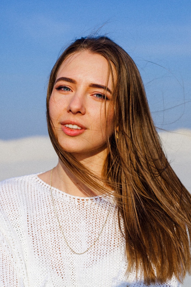 Красивая голубоглазая девушка в белом свитере на фоне голубого неба