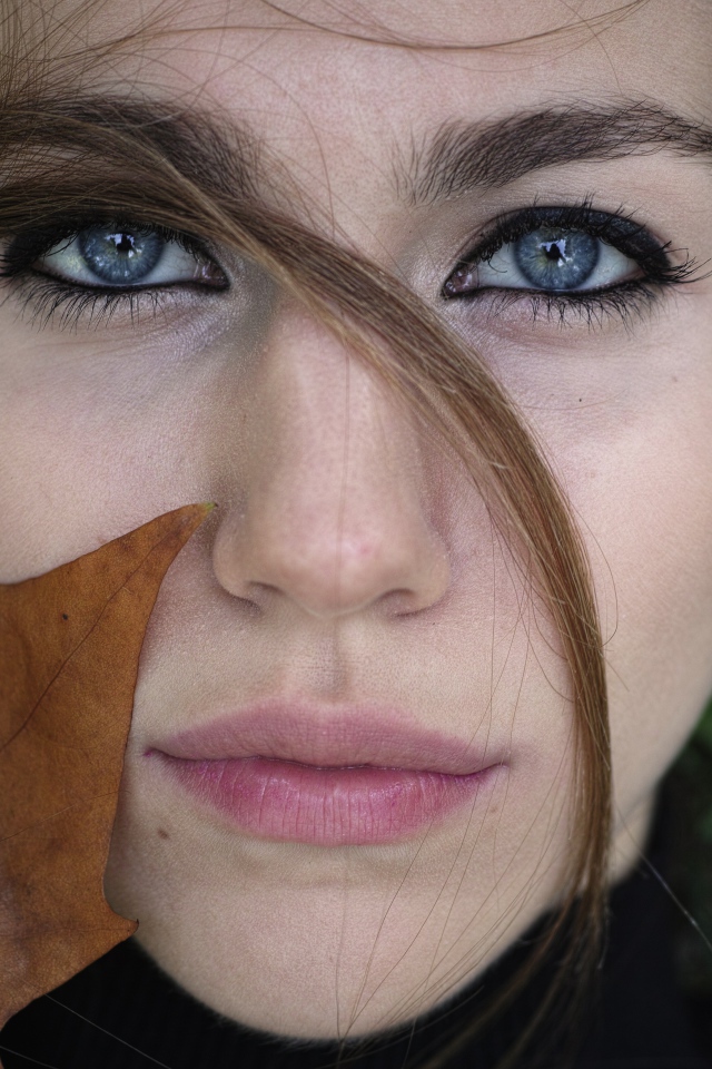 Красивая голубоглазая девушка с желтым листом у лица