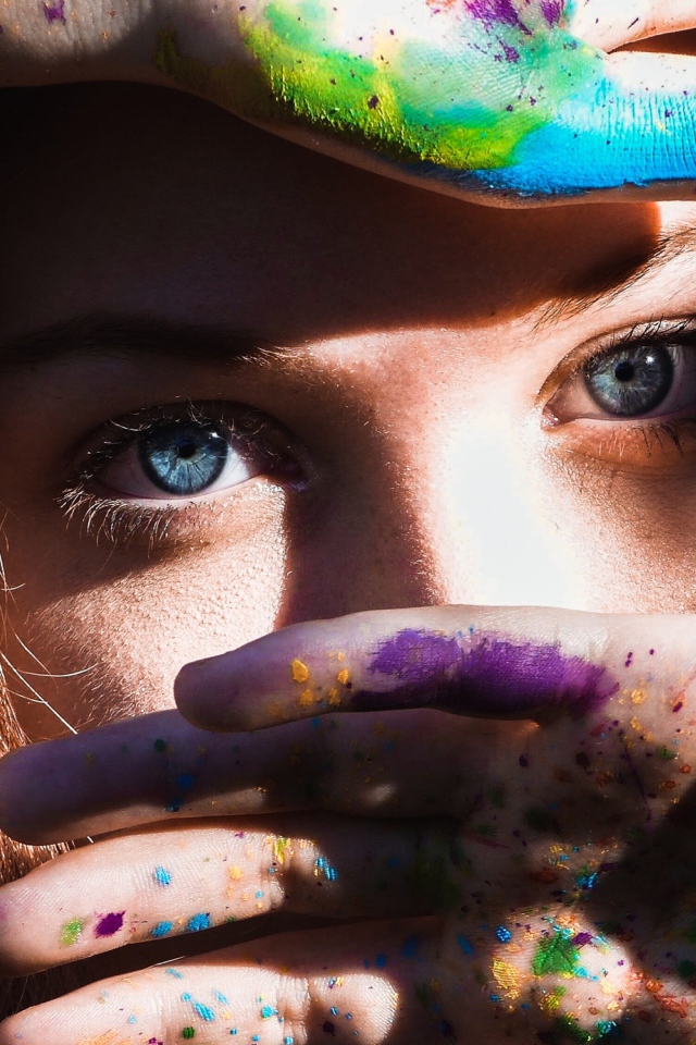 Красивая голубоглазая девушка с руками в разноцветной краске у лица
