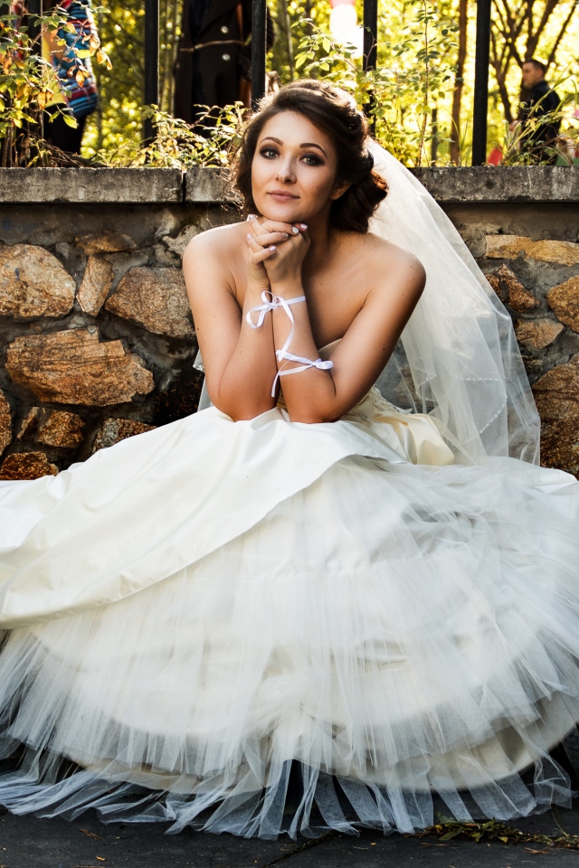 Красивая невеста в белом платье сидит на лавке