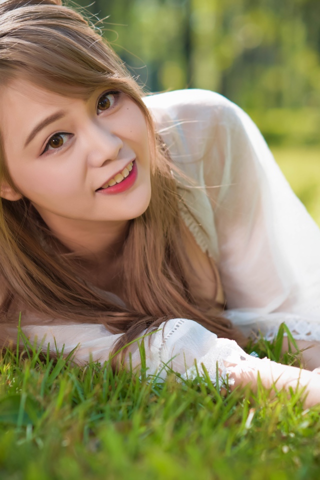 Красивая кареглазая девушка азиатка лежит на зеленой траве