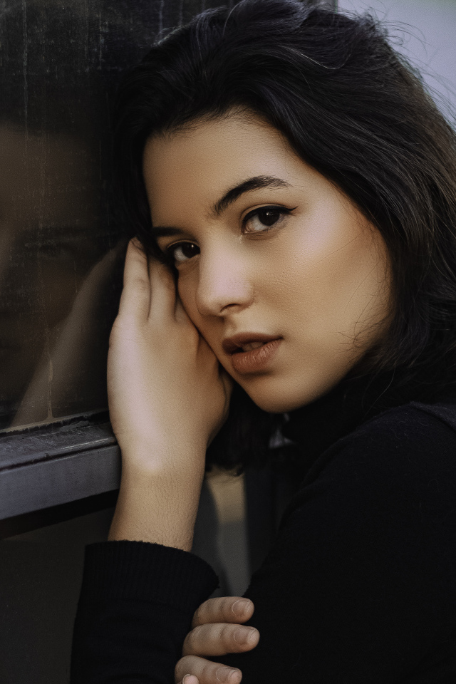 Красивая кареглазая девушка стоит у окна