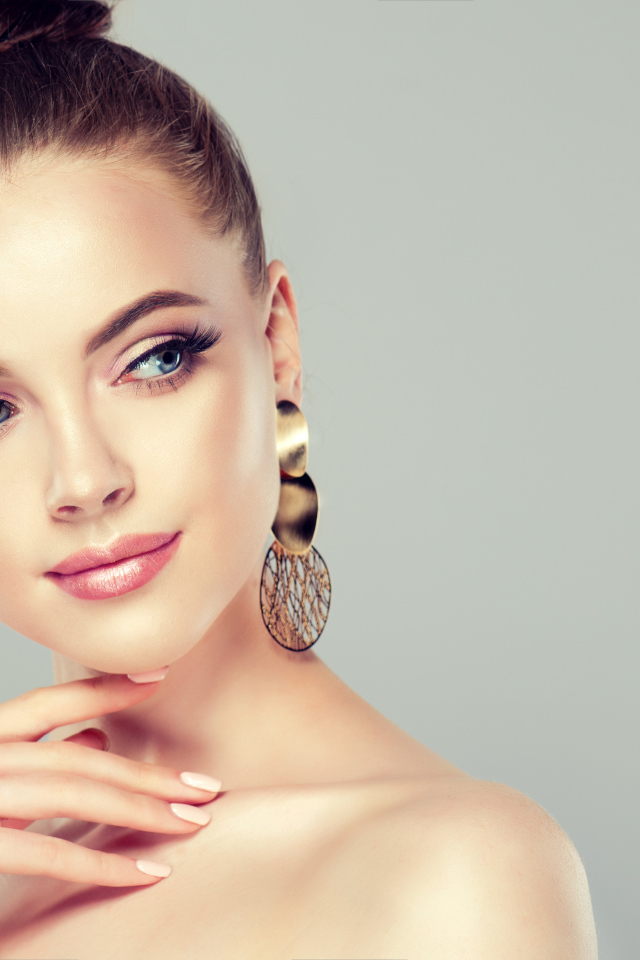 Красивая девушка шатенка с золотыми серьгами в ушах на сером фоне