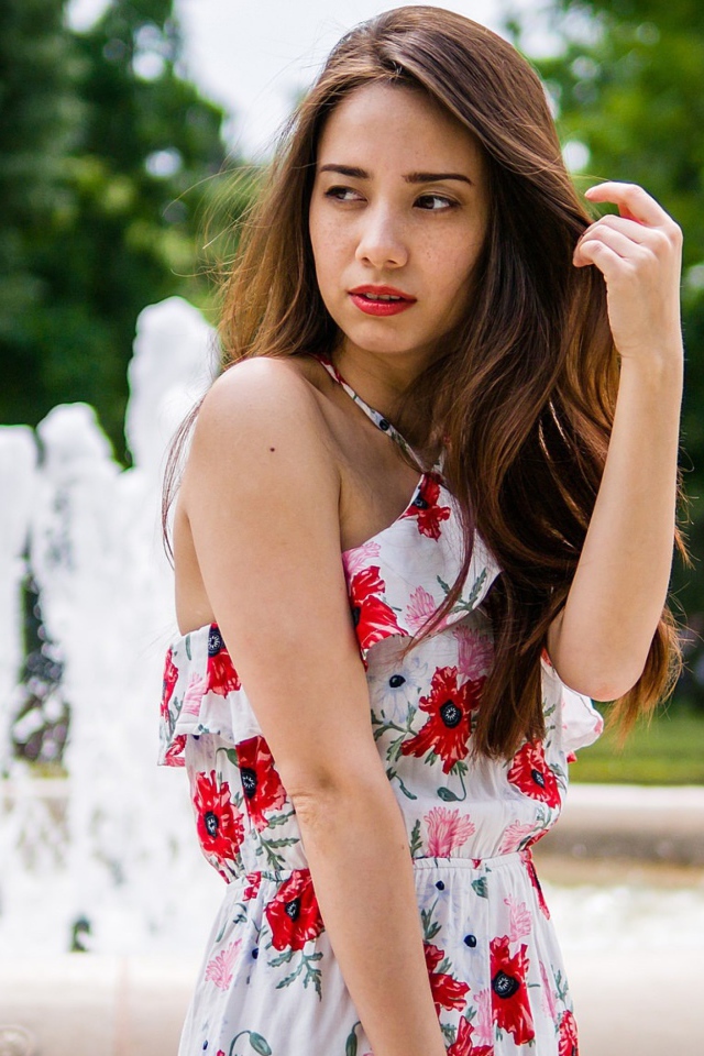 Красивая шатенка в цветастом платье у фонтана летом