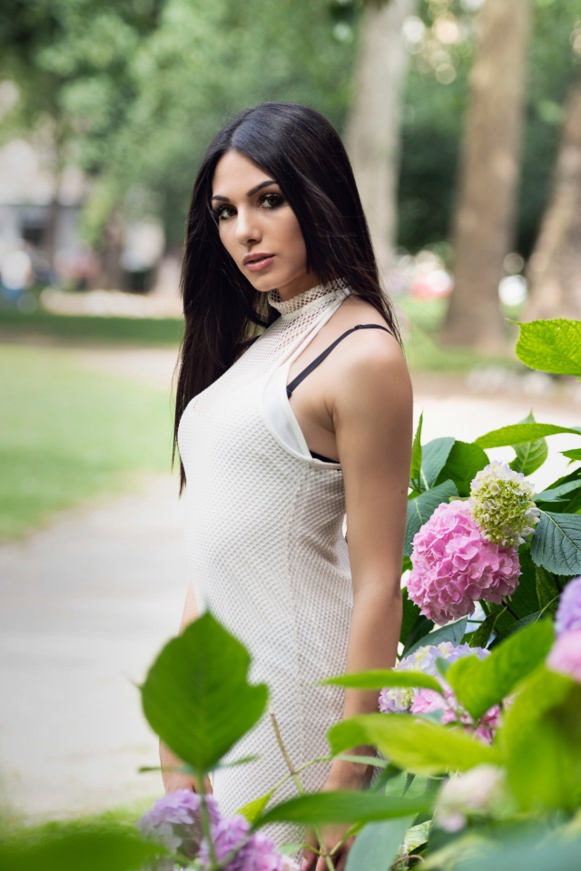 Красивая брюнетка стоит рядом с кустом гортензии