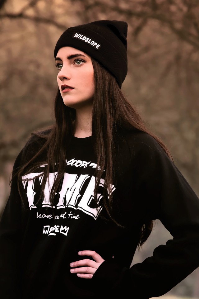 Красивая девушка в черной шапке у деревьев 