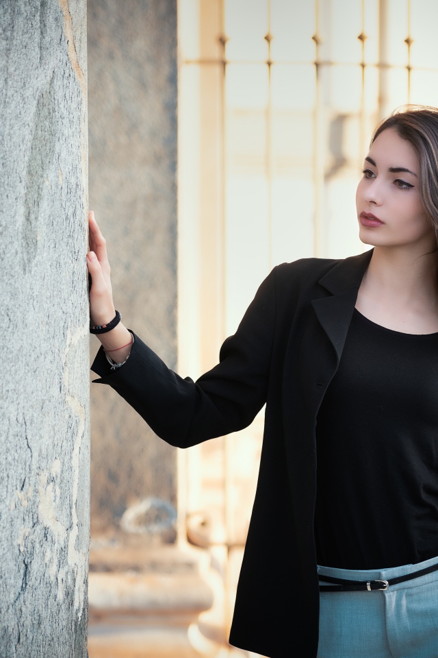 Красивая девушка в черном пиджаке стоит у стены