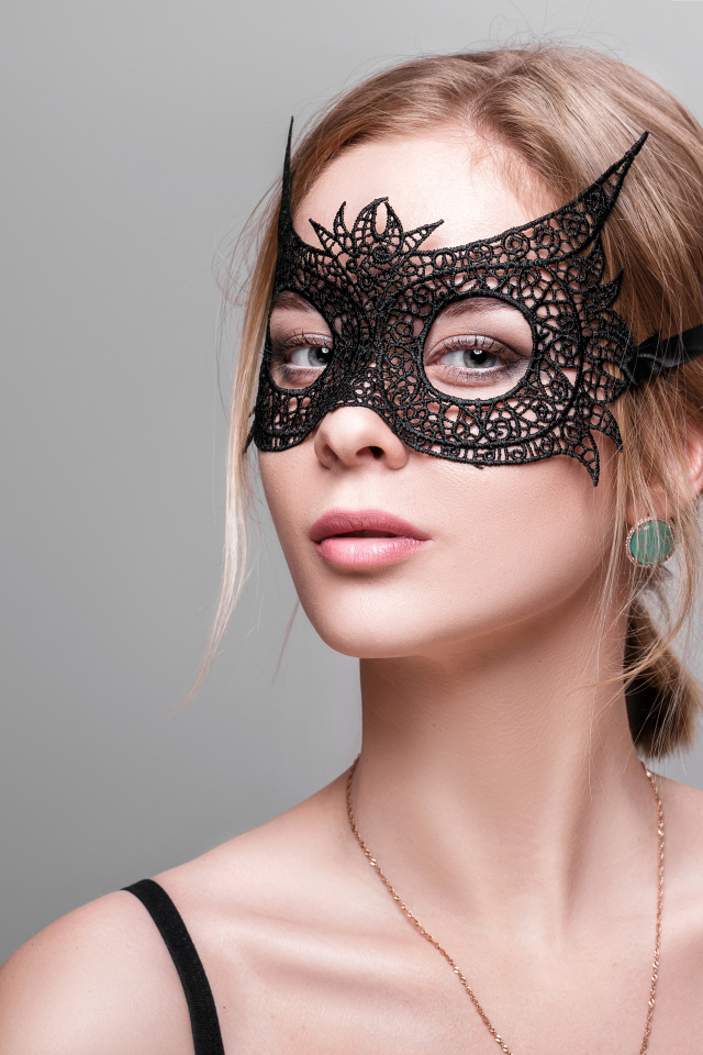 Красивая девушка в черной маске на сером фоне