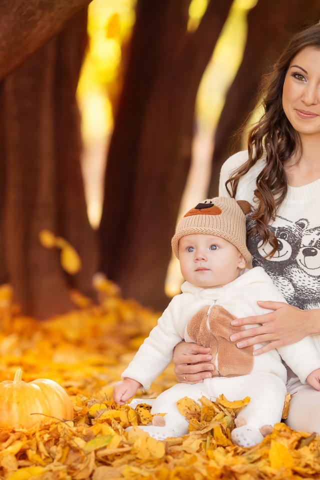 Красивая девушка сидит с грудным ребенком на опавшей листве