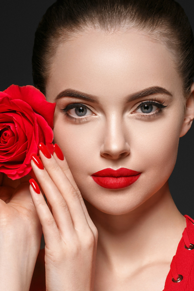 Красивая девушка с красной розой у лица на сером фоне