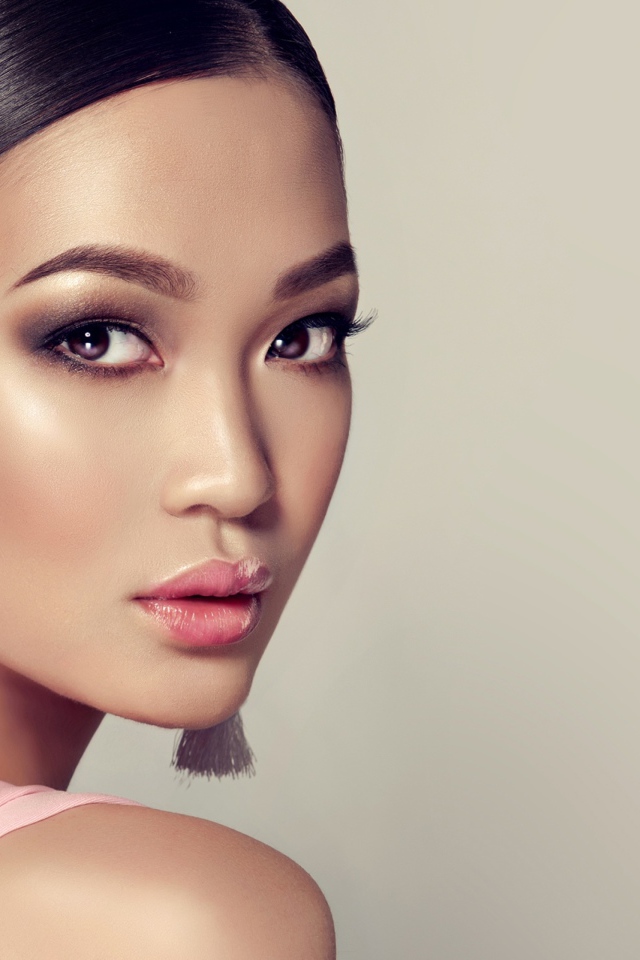 Красивая девушка с прической и сережками в ушах на сером фоне