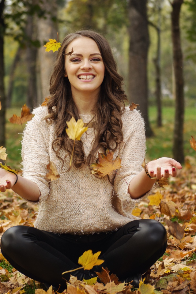 Красивая улыбающаяся девушка сидит на земле с желтыми листьями