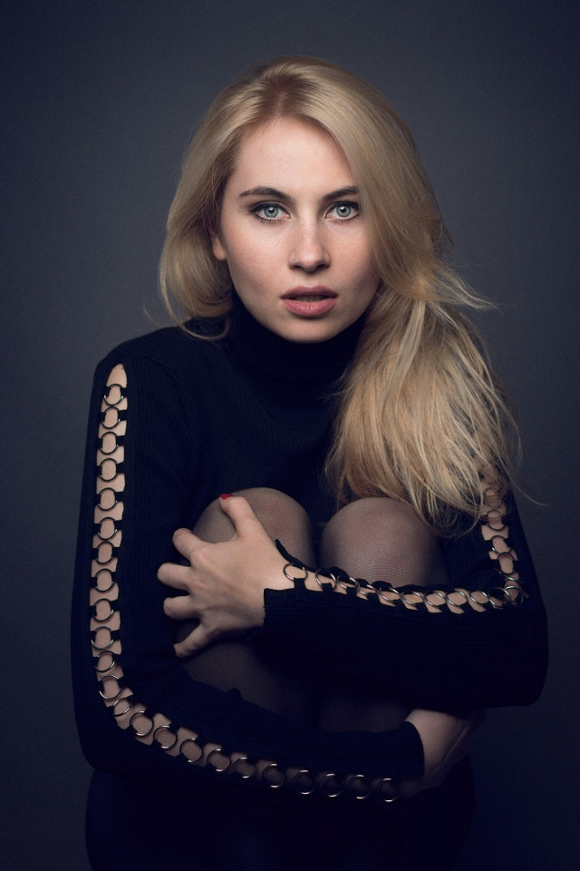 Блондинка в черном наряде на сером фоне