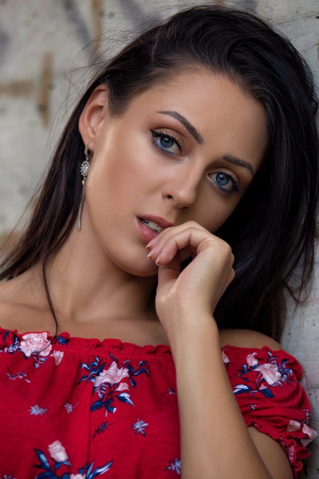 Голубоглазая брюнетка стоит в платье стоит стены