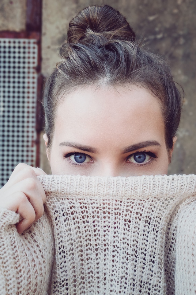 Голубоглазая девушка закрыла лицо свитером 