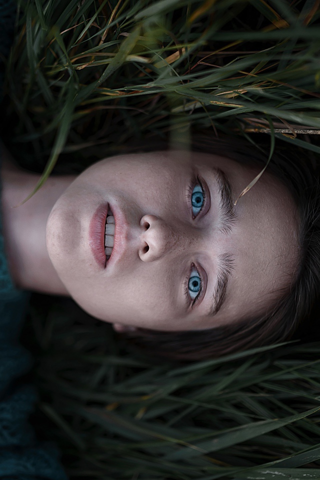 Голубоглазая девушка в свитере лежит на траве