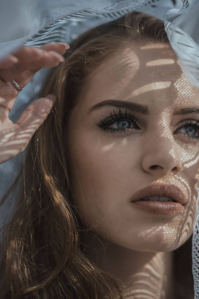 Голубоглазая девушка смотрит в окно с тюлью