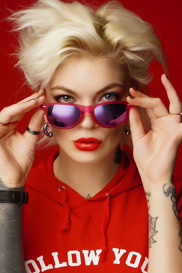 Яркая блондинка с татуировками на руках на красном фоне