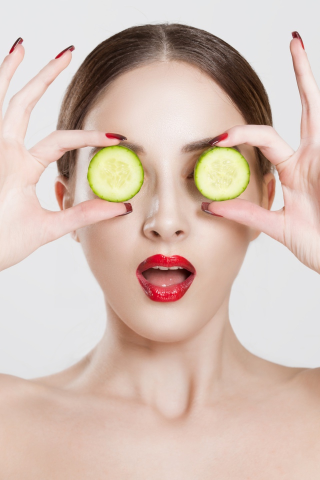 Яркая девушка с огурцами у глаз на сером фоне