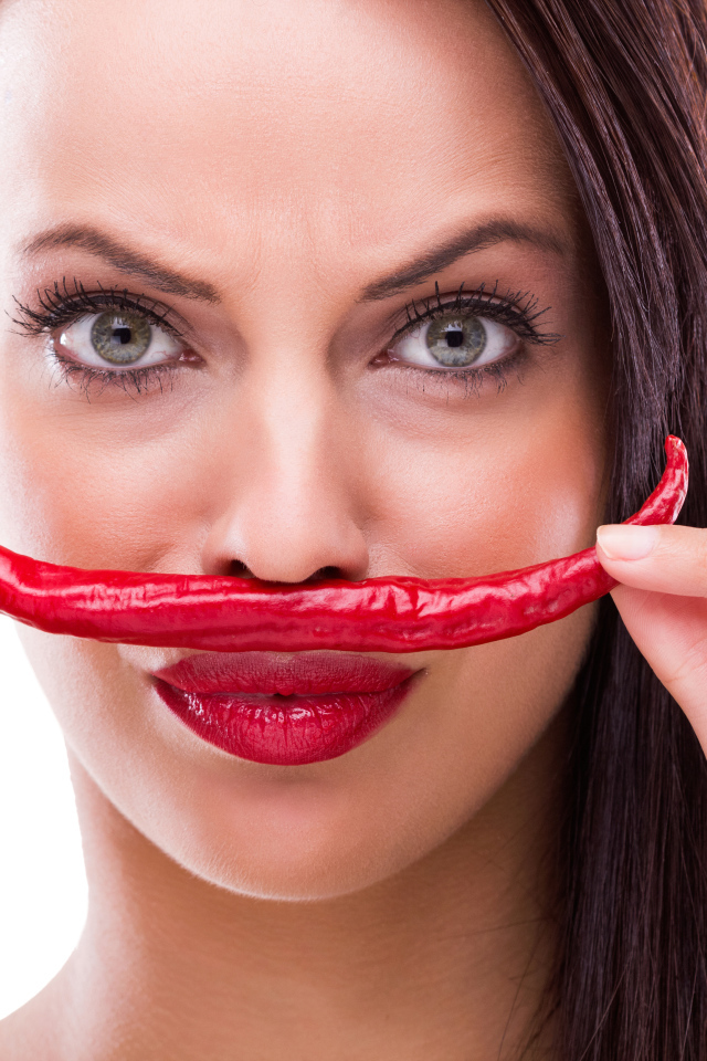 Брюнетка с красным перцем у лица на белом фоне