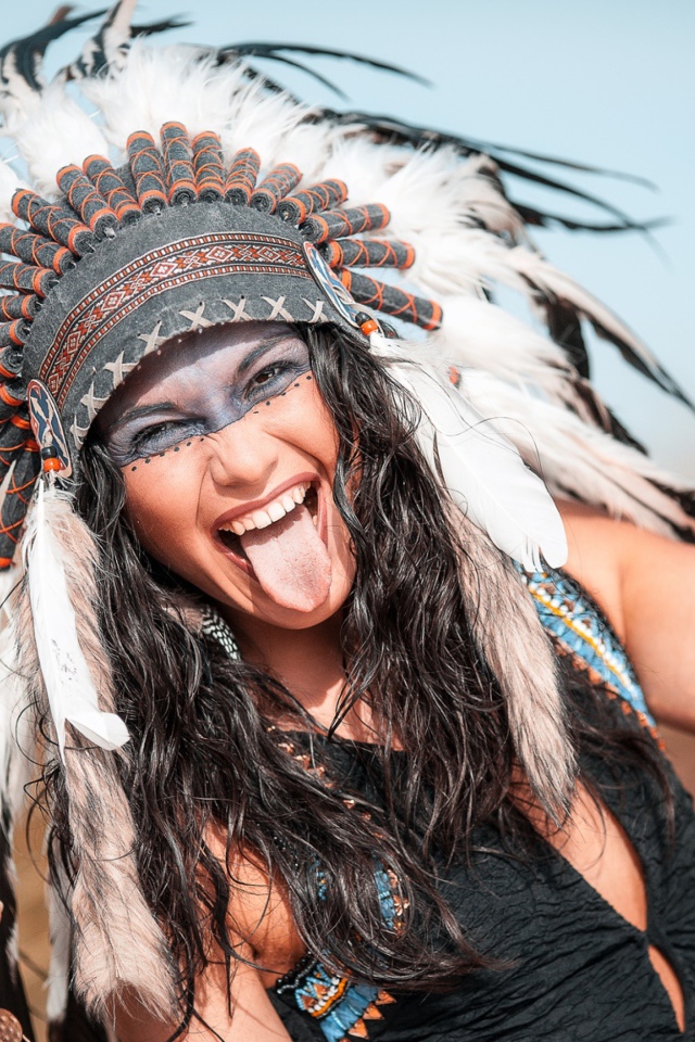 Веселая девушка с высунутым языком в костюме индейца