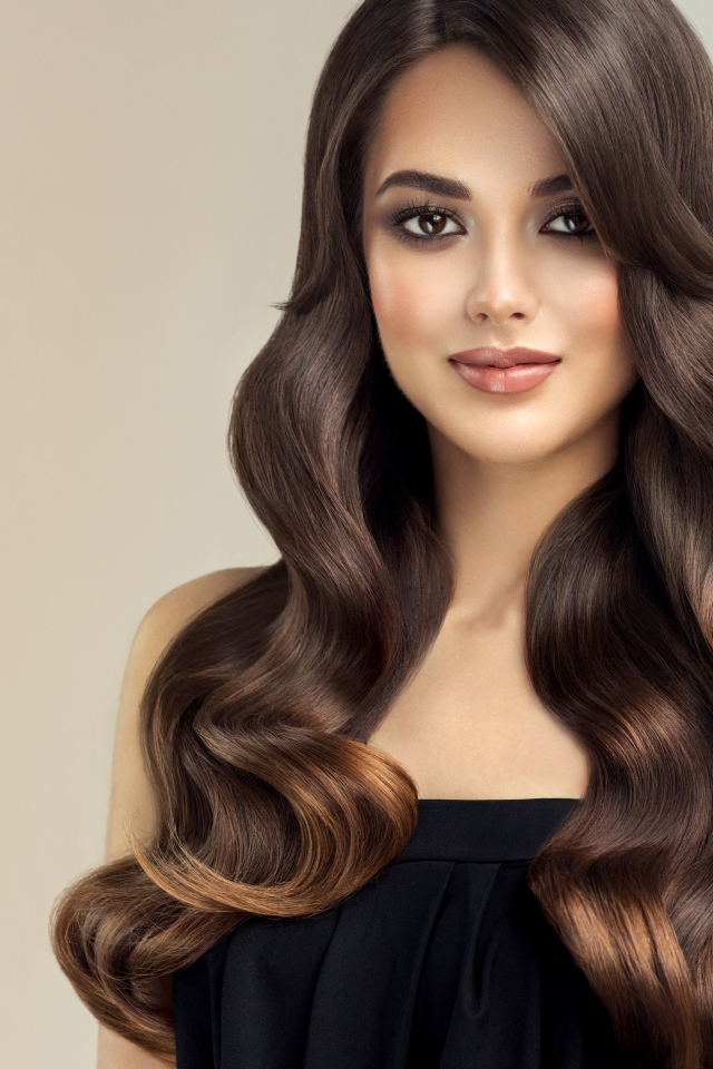 Милая кареглазая девушка с красивыми длинными волосами на сером фоне