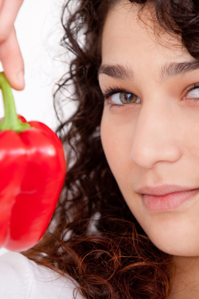 Лицо девушки с красным сладким перцем в руке крупным планом