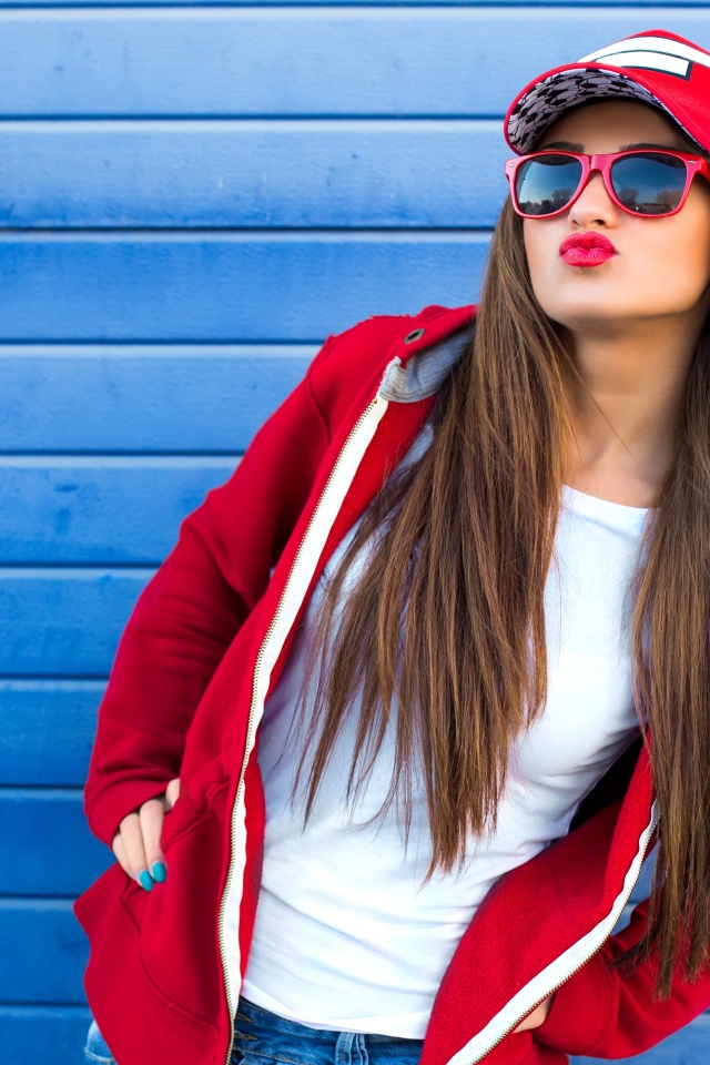 Девушка в бейсболке и солнечных очках у стены