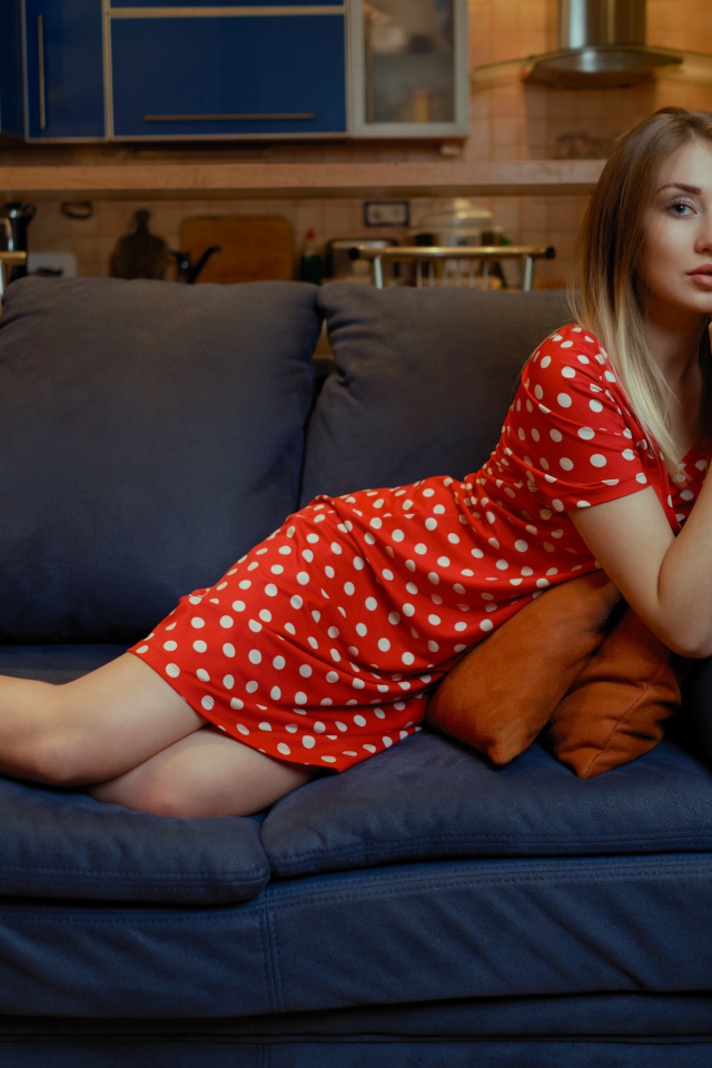 Девушка в красном платье в горошек лежит на диване