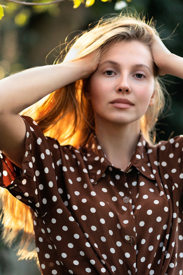 Девушка в рубашке в горох с руками в волосах 