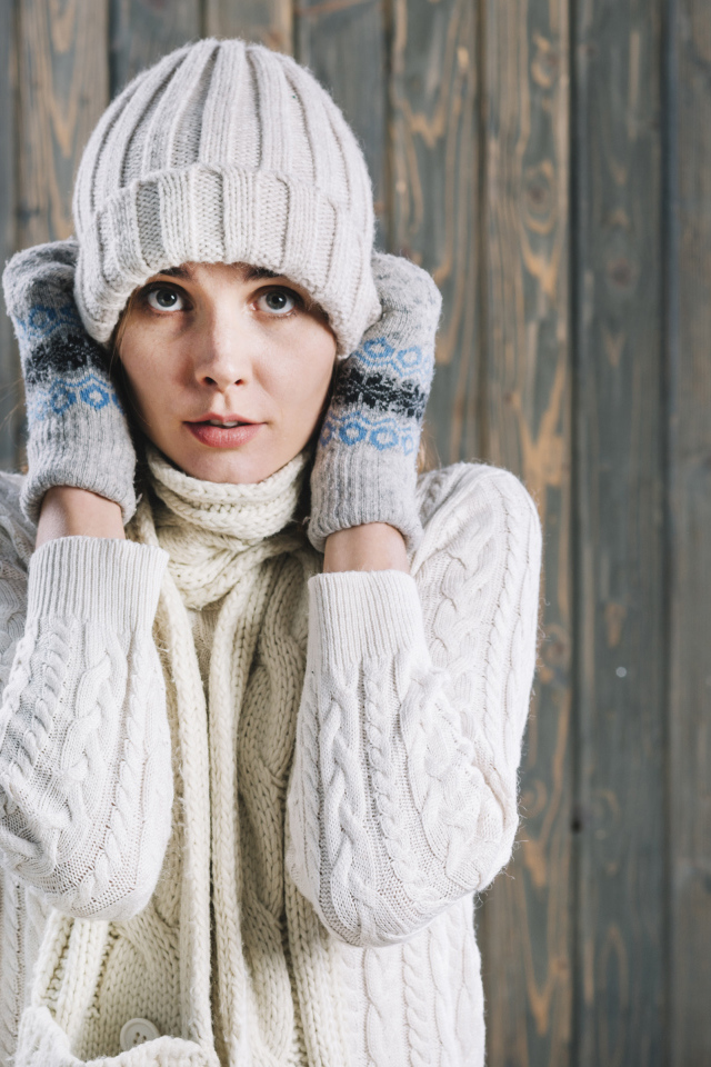 Девушка в варежках поправляет шапку на голове