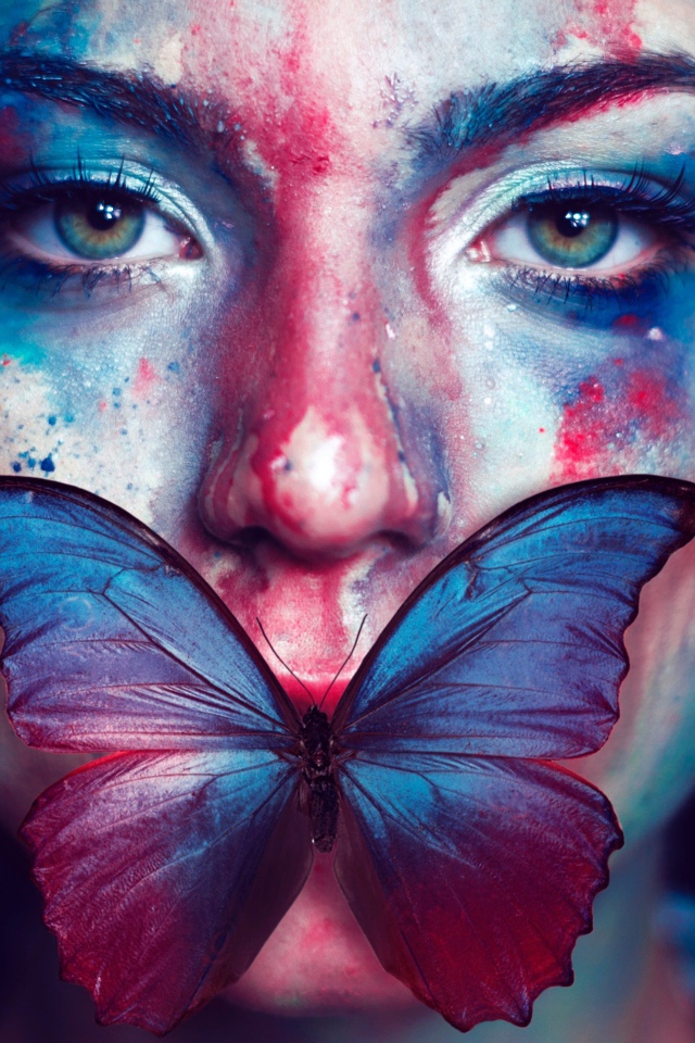Лицо девушки в краске с бабочкой во рту