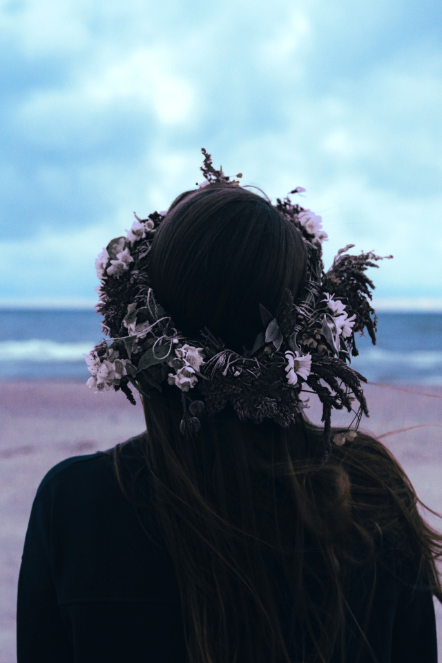 Девушка с венком на голове на фоне моря вид сзади