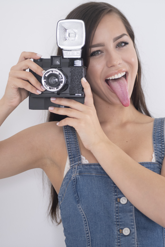 Девушка с высунутым языком с фотоаппаратом в руках