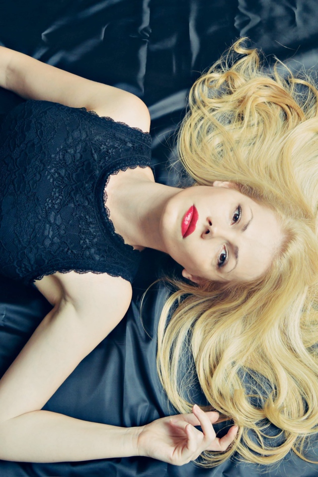 Длинноволосая блондинка в черном платье лежит на кровати