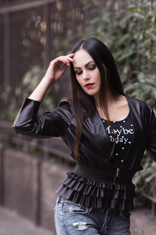 Длинноволосая брюнетка в черной куртке у забора