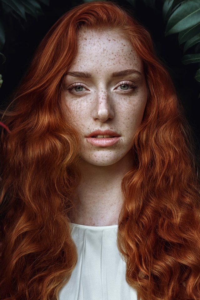 Рыжеволосая девушка с веснушками на лице на фоне кустов 