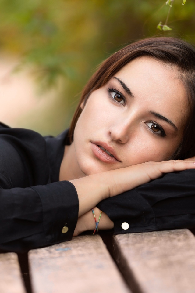 Грустная кареглазая девушка лежит на деревянной лавке