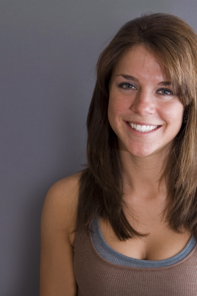 Улыбающаяся милая девушка у серой стены