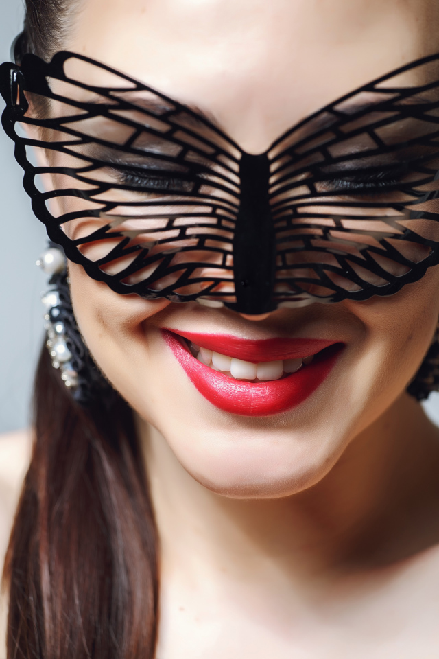 Улыбающаяся девушка в черной маске на сером фоне