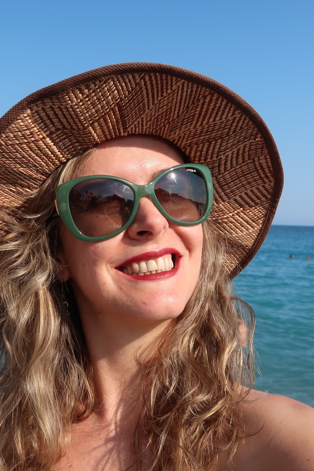 Улыбающаяся девушка в солнечных очках и шляпе на море