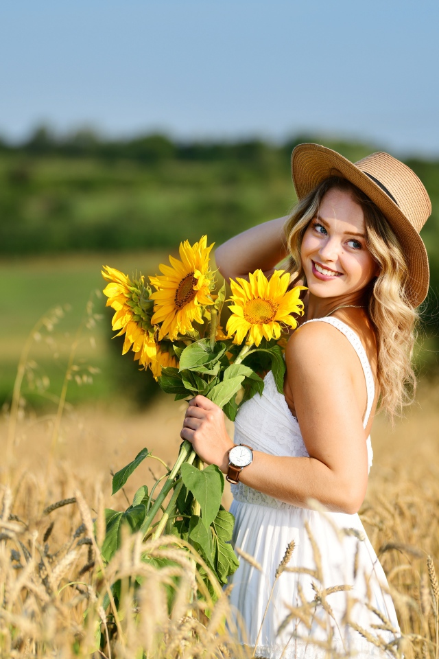 Улыбающаяся девушка на поле с пшеницей с букетом подсолнухов в руке