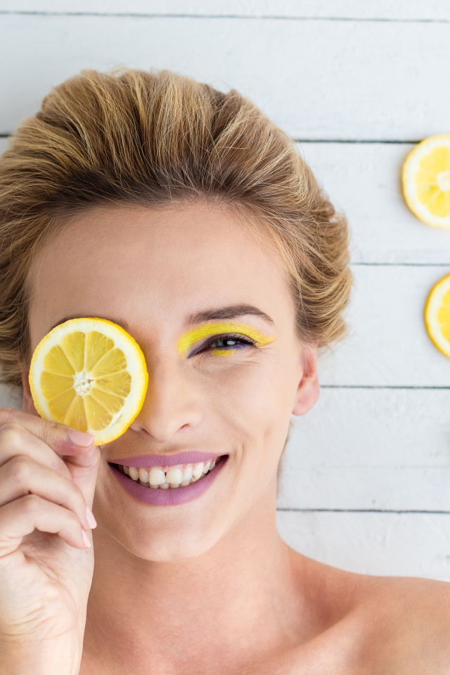 Улыбающаяся девушка приложила лимон к глазу