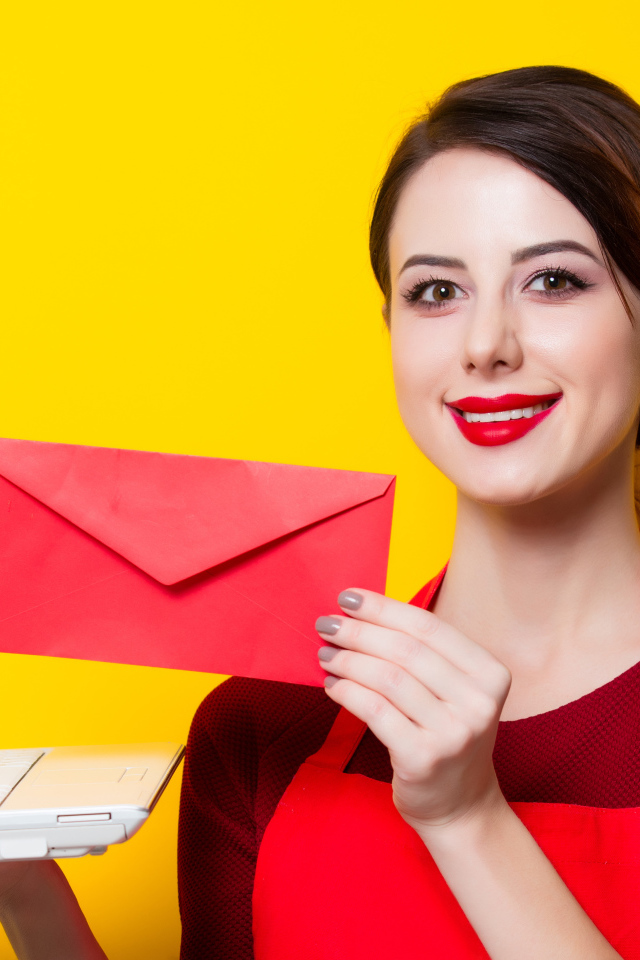 Улыбающаяся девушка с ноутбуком и конвертом в руках на желтом фоне