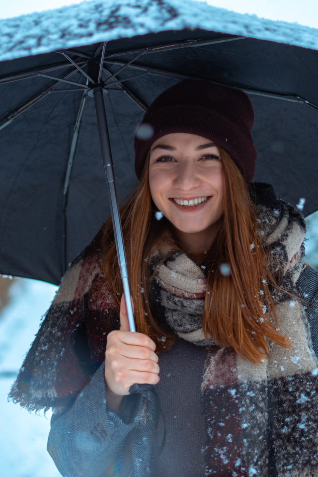 Улыбающаяся молодая девушка под зонтом зимой