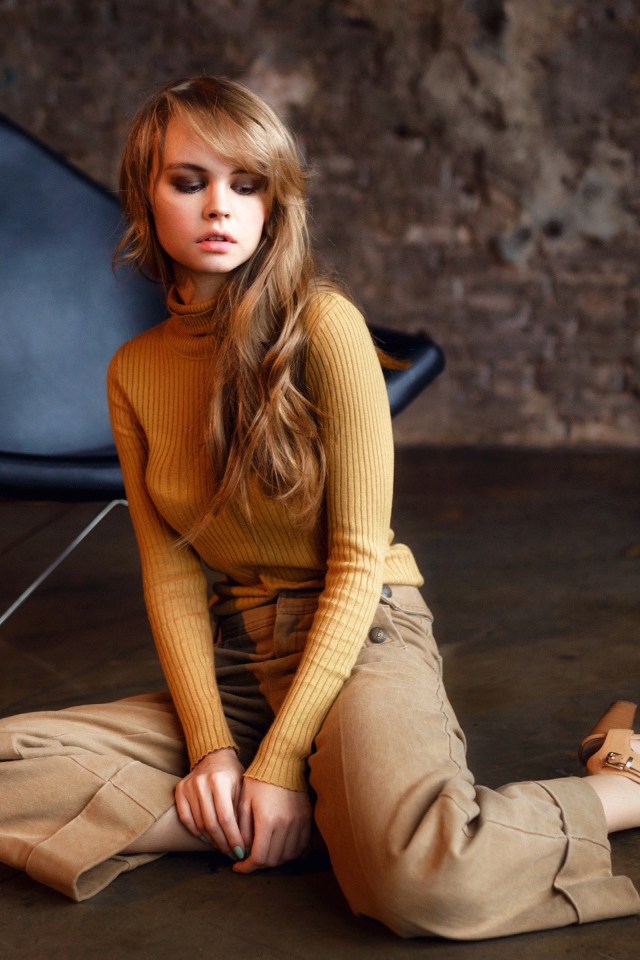 Девушка сидит на полу около черного кресла 